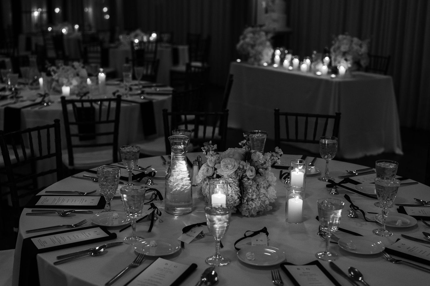 Elegant candlelit dinner tables with glass centerpieces in a dimly lit wedding reception