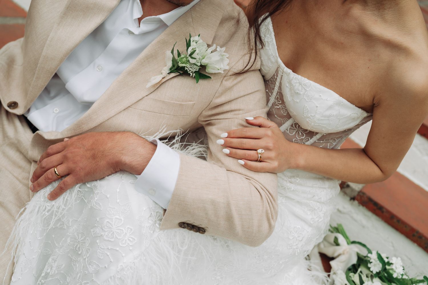 Wedding celebration showing hands resting on a cream-colored formal outfit with delicate floral decorations.