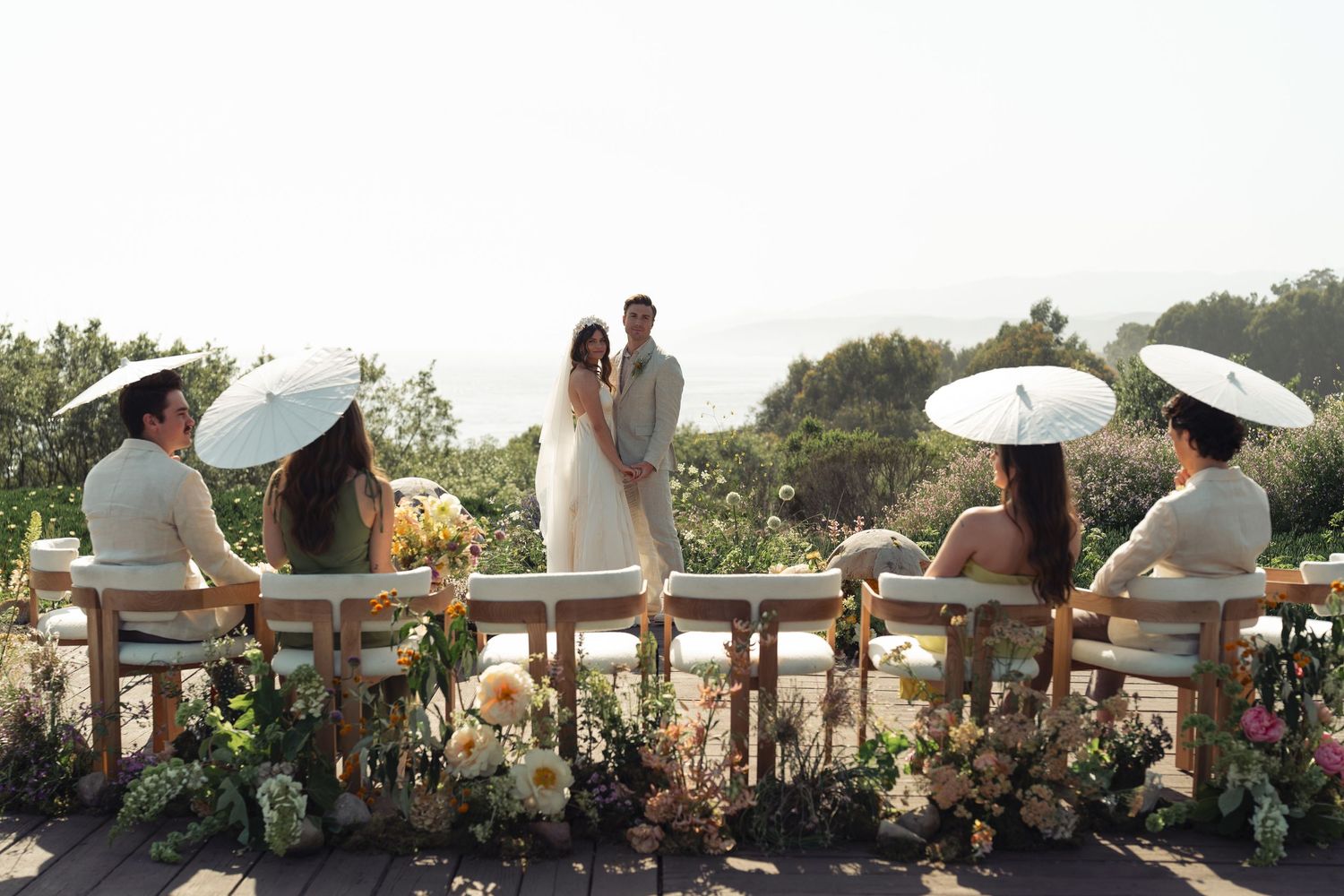 Wedding couples looks at guests with white umbrellas during an outdoor ceremony at sunset in California