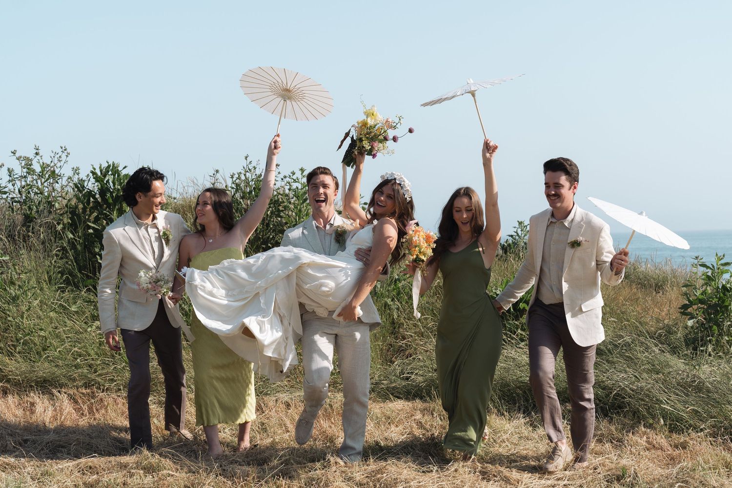 Wedding party  jumps joyfully with parasols against a sunny outdoor landscape in California