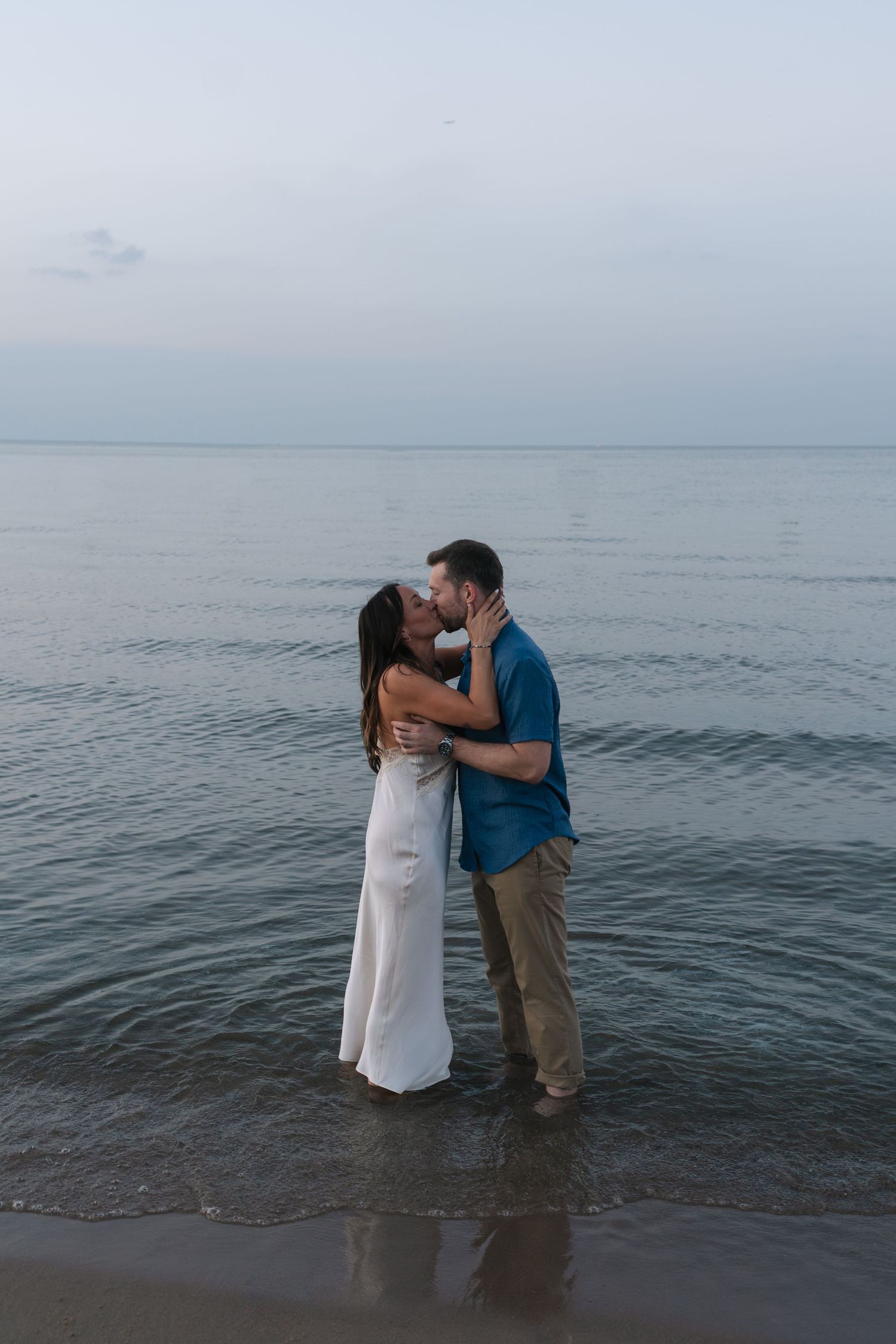 A romantic couple shares an intimate moment while standing in the shallow waters Lake Michigan of a serene beach at dusk.