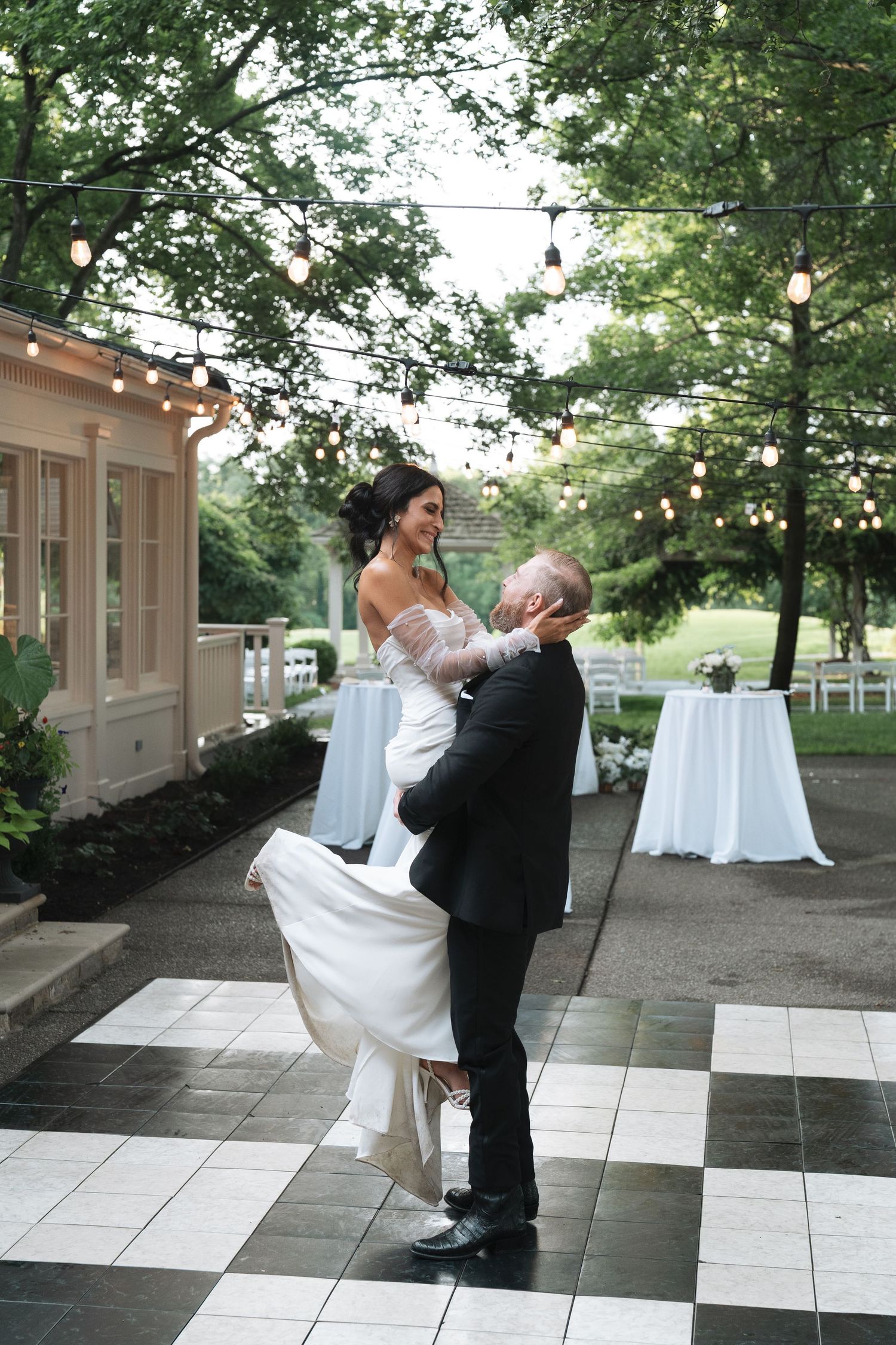 A couple dancing together in a joyful dance sequence on an outdoor patio with string lights overhead in Nashville, Tennessee