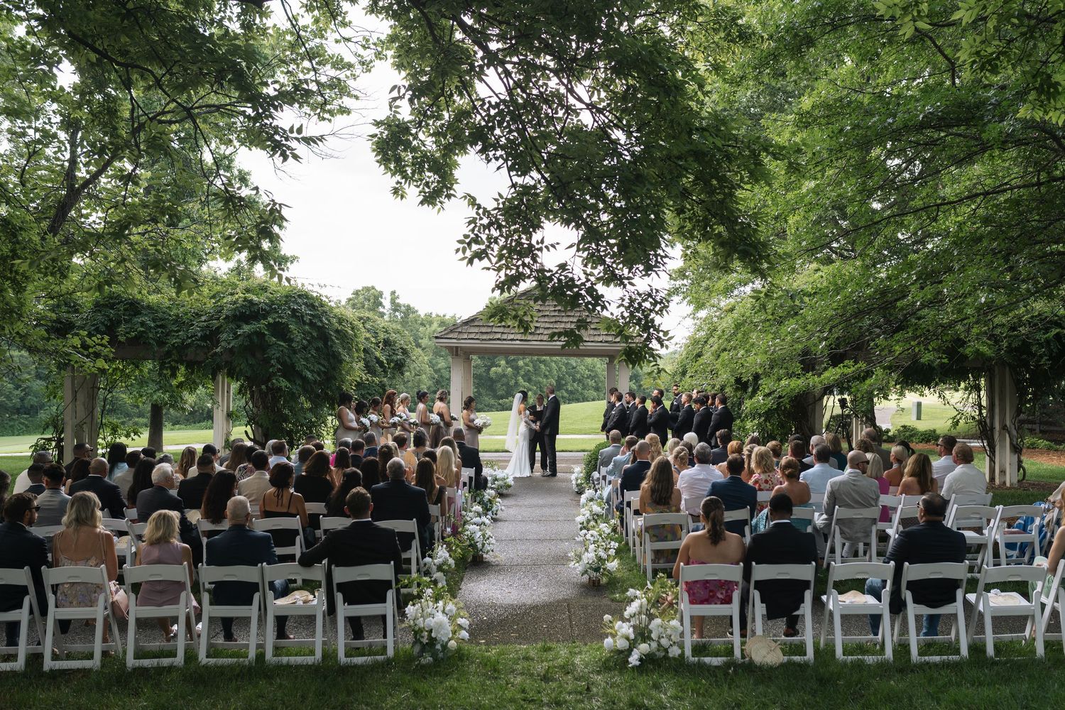 Outdoor wedding ceremony setup with white folding chairs arranged in rows under tall green trees in Nashville, Tennessee