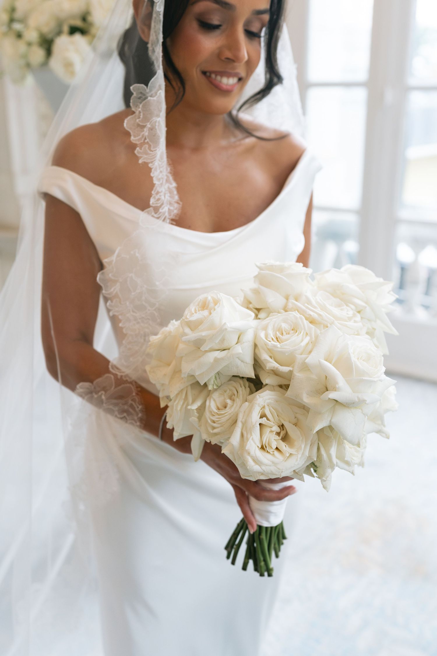 Bride in off-shoulder white gown and lace veil holds elegant bouquet of white roses on her wedding day at the Hermitage Hotel in Nashville.