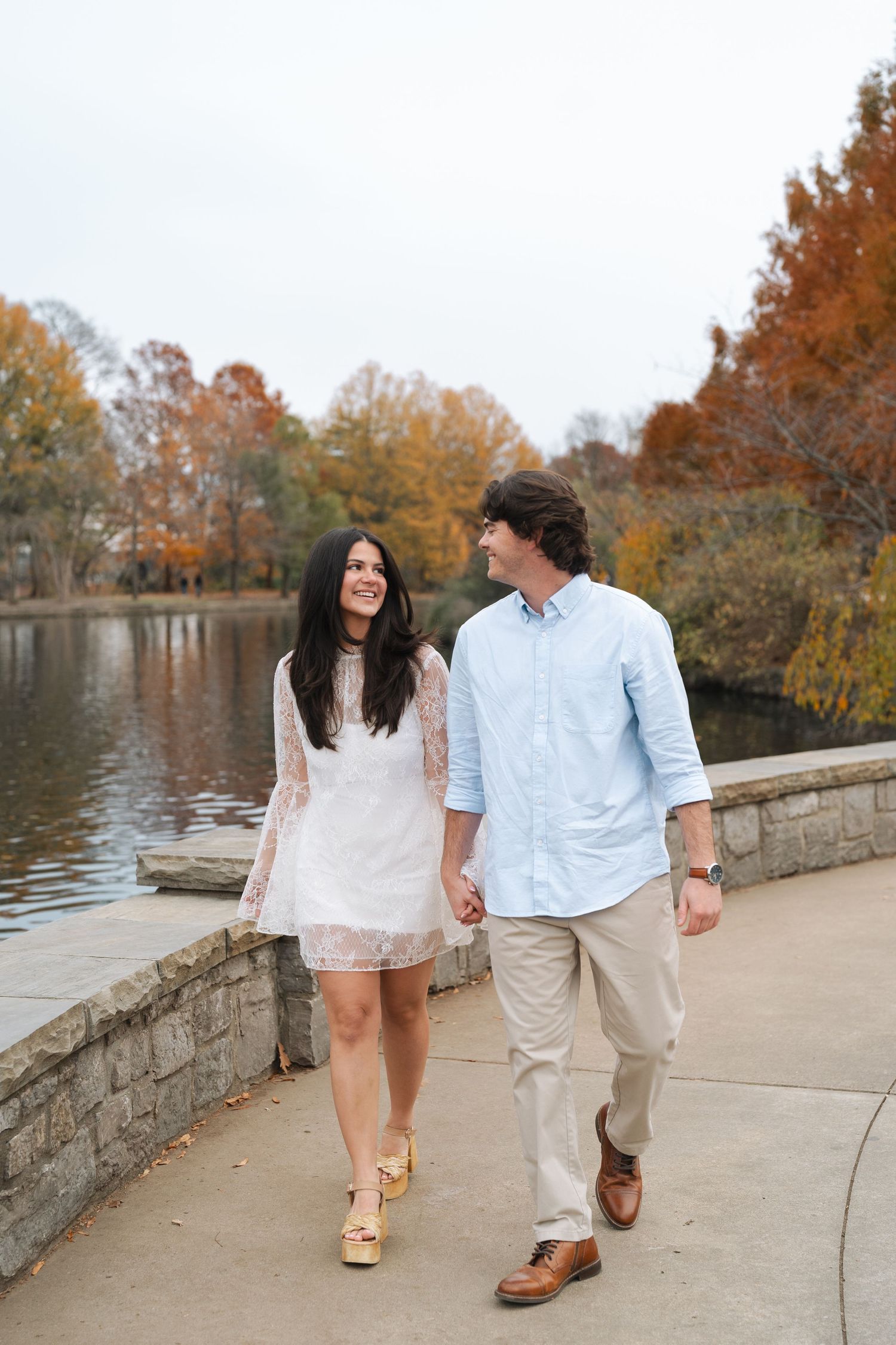 A couple walks along a stone pathway by a pond during autumn with colorful fall foliage in Nashville