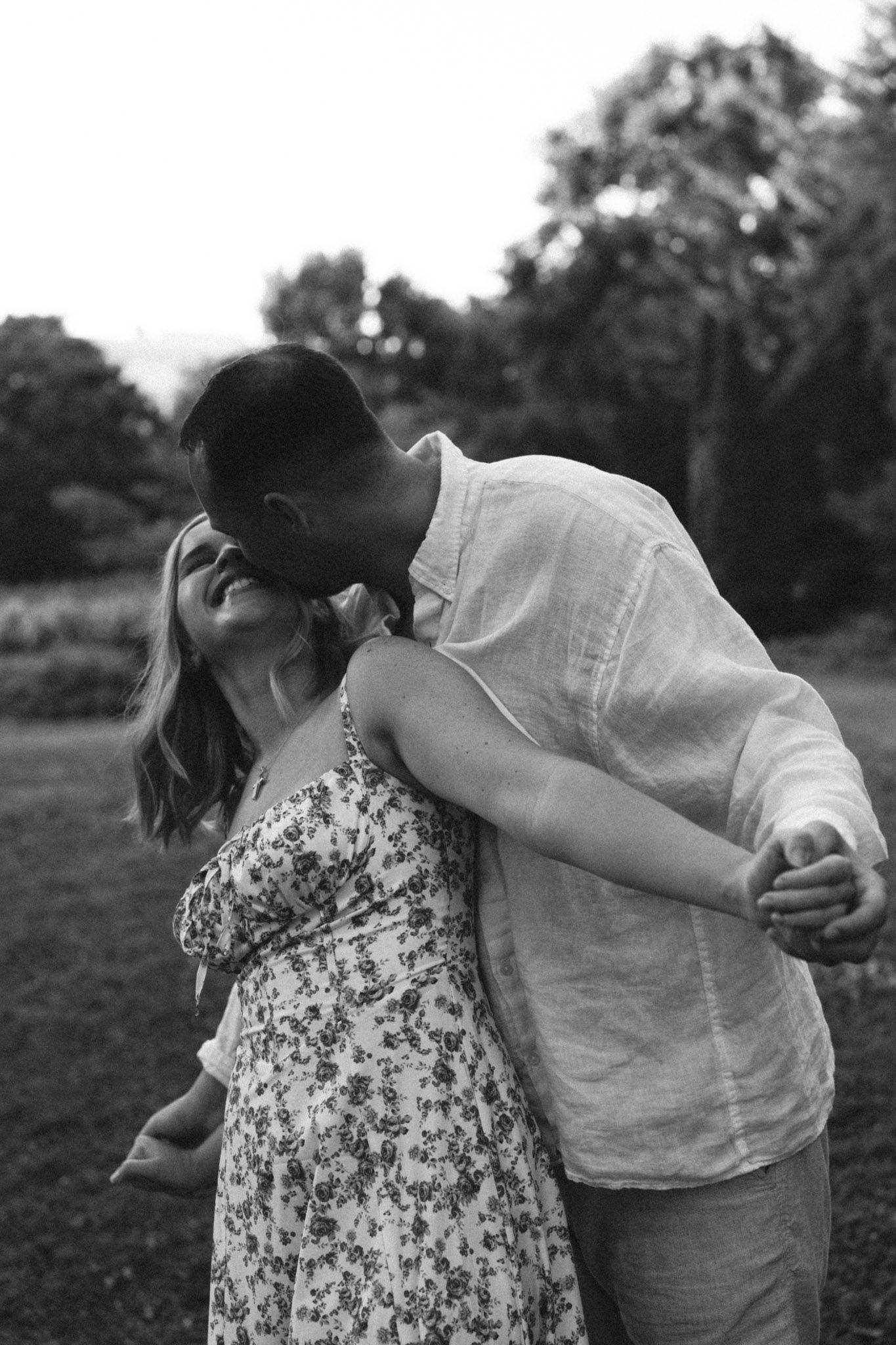 A romantic black and white photograph shows a couple sharing an intimate kiss outdoors in Centennial Park