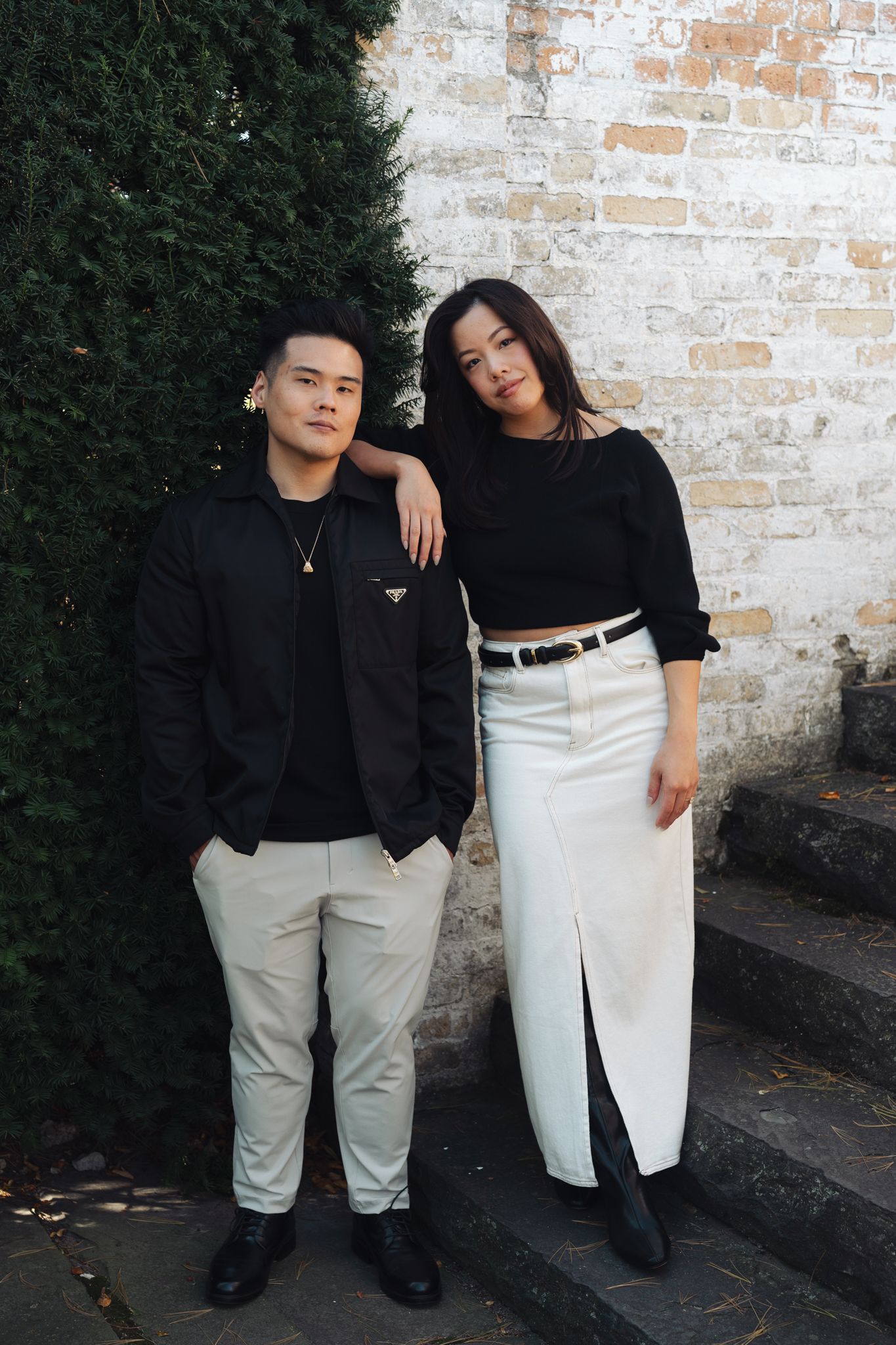 A couple in coordinated black and white outfits poses against a brick wall at Villa Terrace.