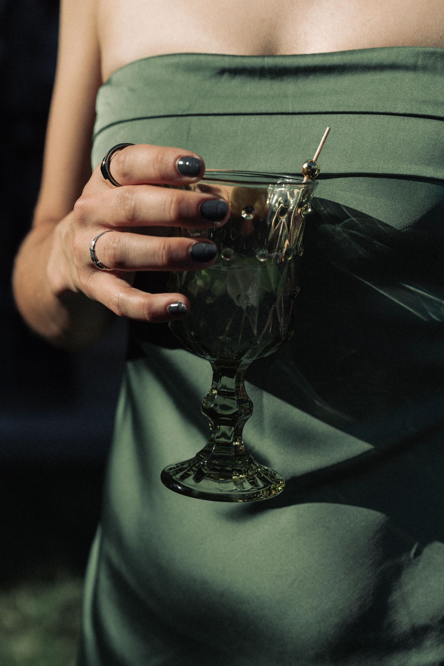 Hands hold a vintage glass goblet against an emerald green satin dress background.