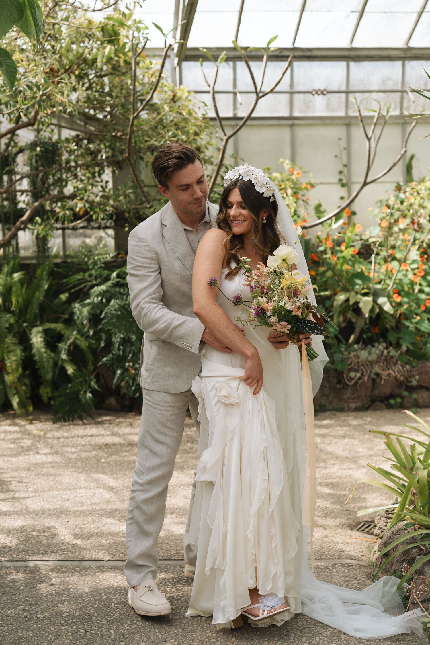 A couple in wedding attire shares intimate moments in a greenhouse garden setting during their special day in California