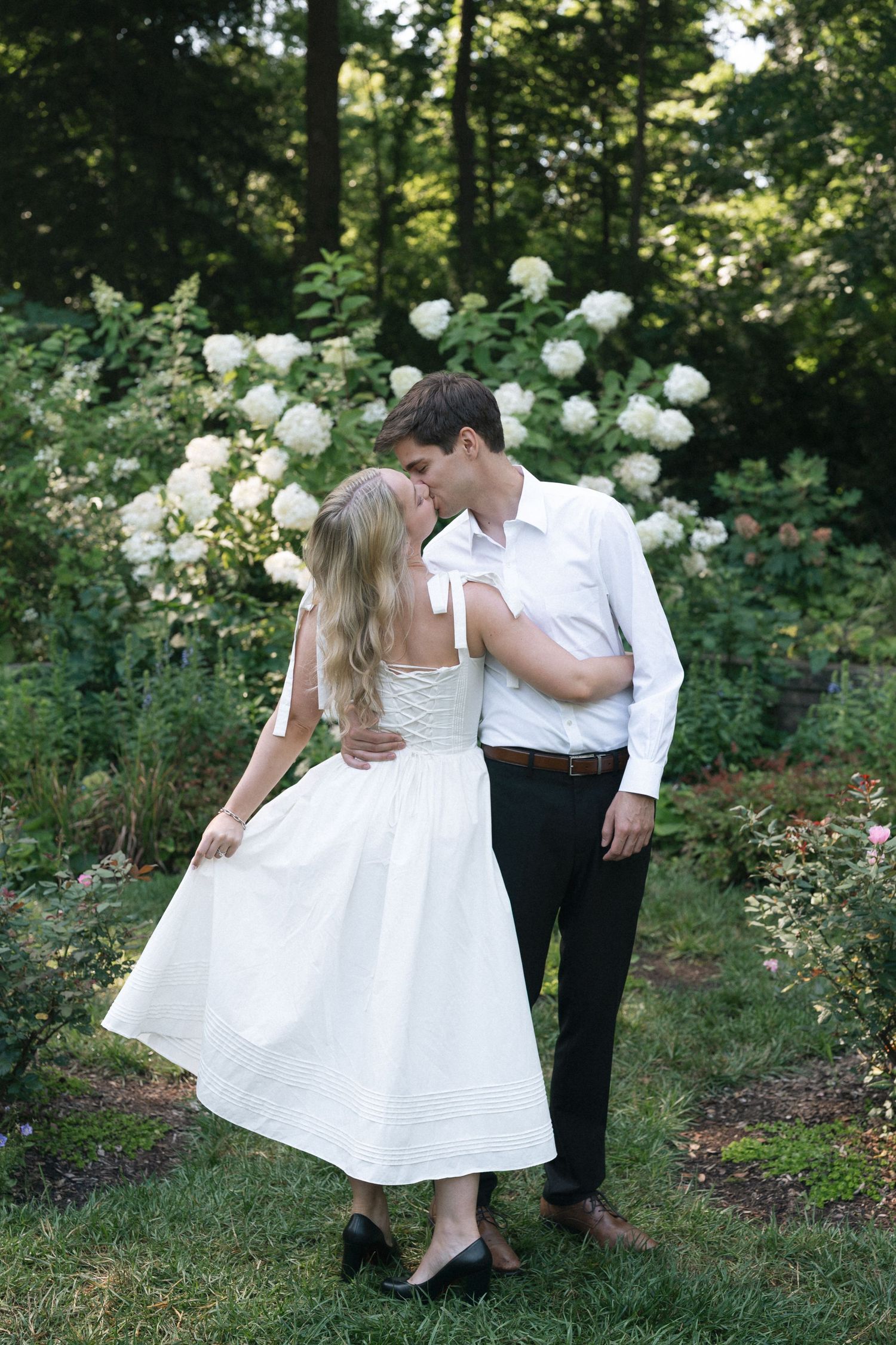 Romantic couple in white and dark attire dance together in a lush garden setting with white flowers in Indianapolis