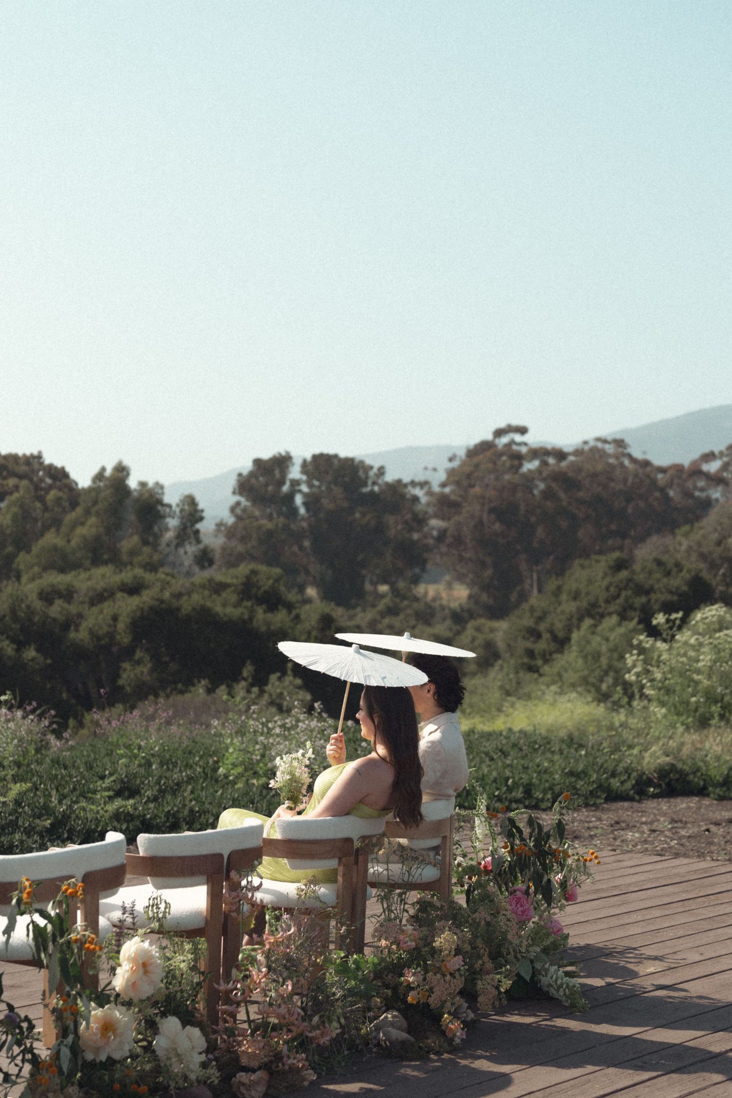 A scenic garden terrace with white floral arrangements and outdoor seating overlooking a lush mountain landscape