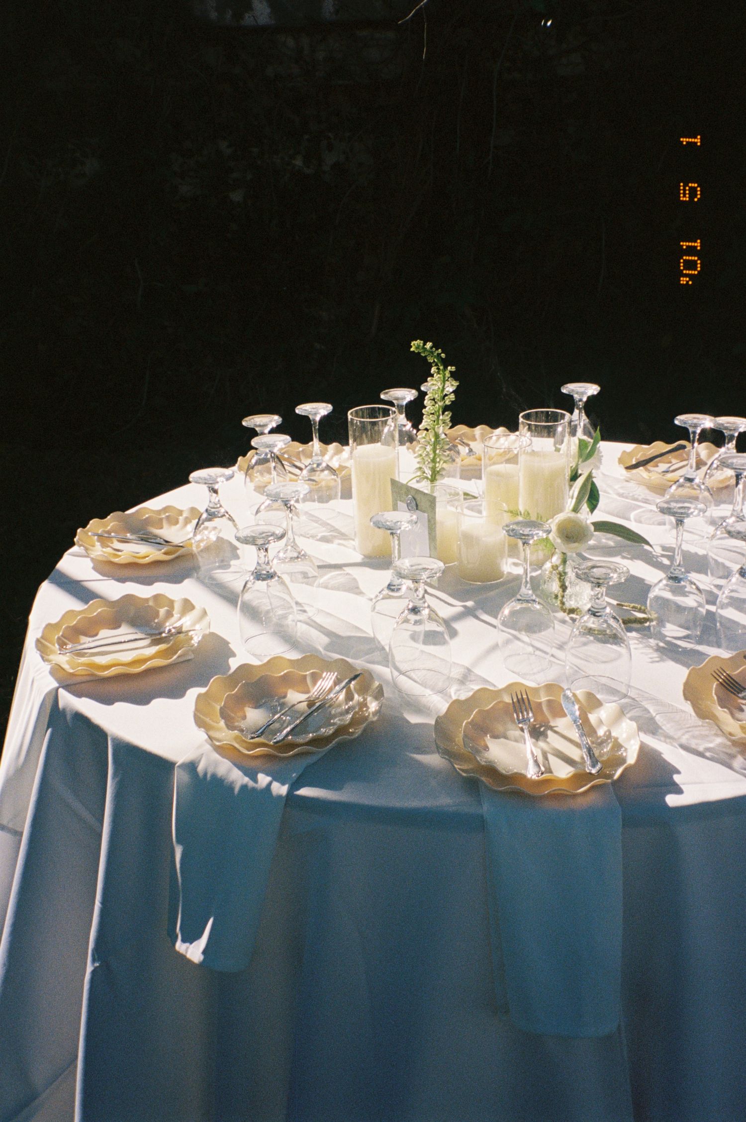 Elegant table setting with gold plates and white linens features delicate glassware and simple floral centerpiece in Florida