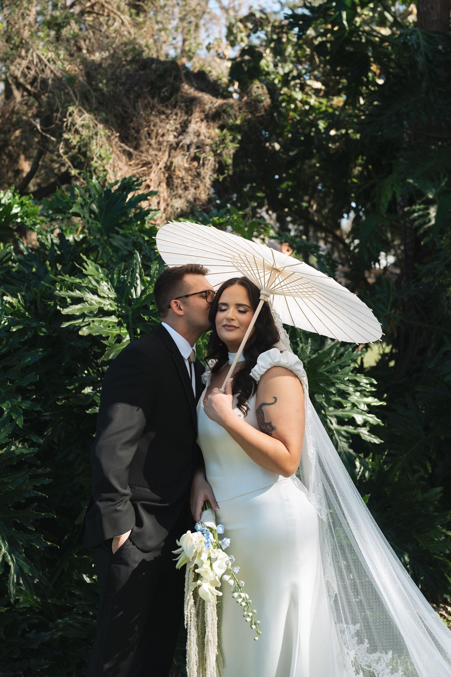 Romantic wedding couple shares intimate moments under white parasol umbrella in lush garden setting in Tampa, Florida