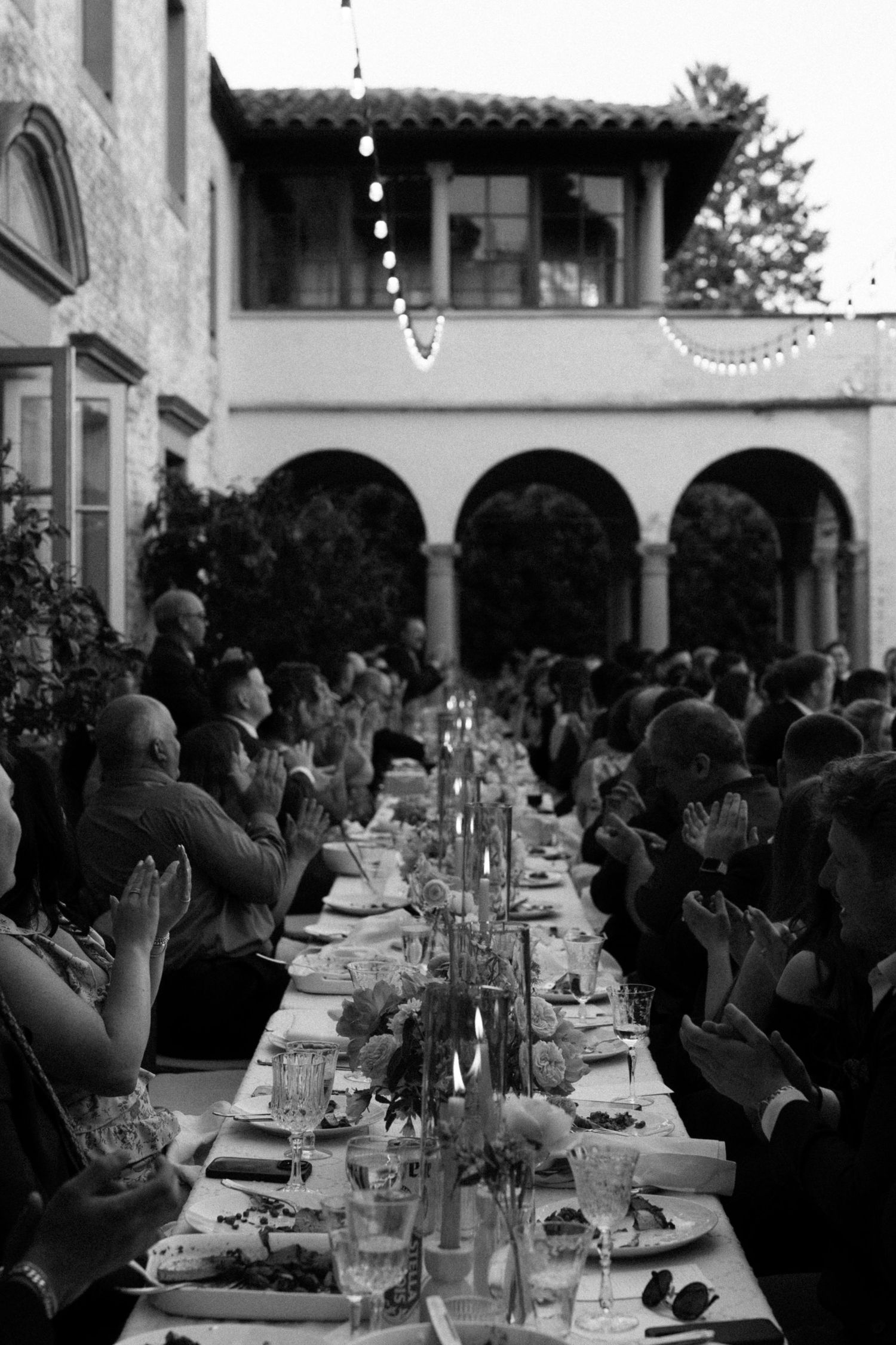 Guests gather around a long outdoor dining table for an elegant reception under covered Italian archways