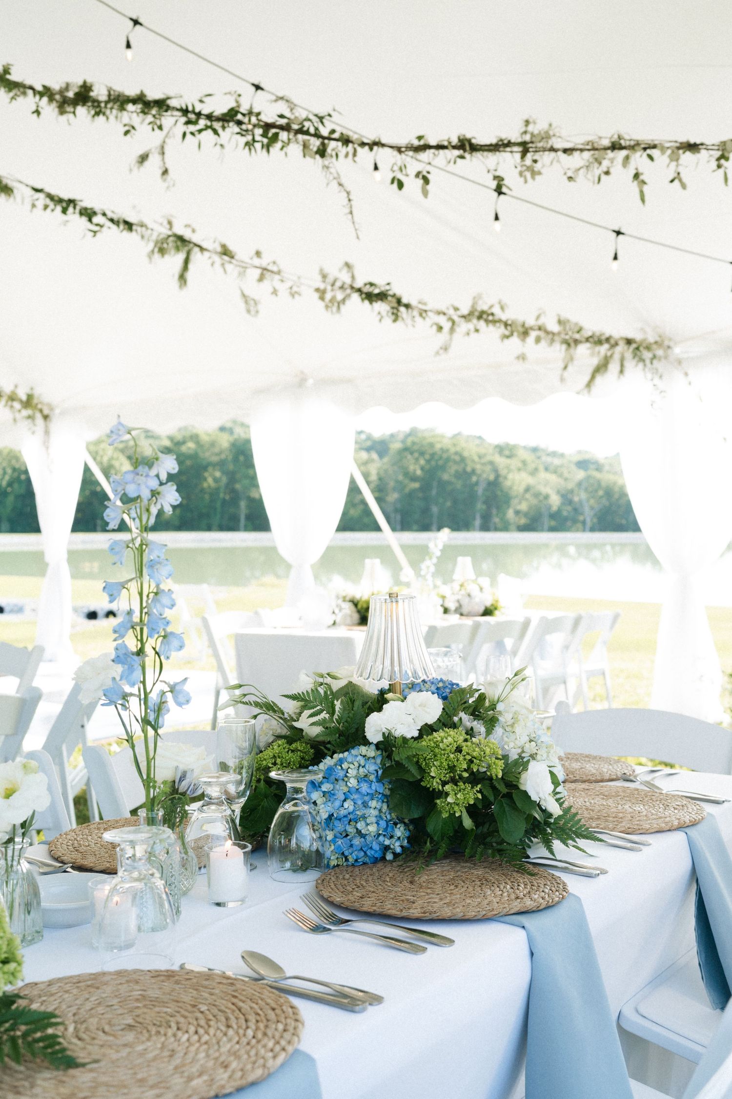 Elegant outdoor wedding reception tent with blue hydrangea centerpieces, woven placemats, and floral garland ceiling decor in Illinois