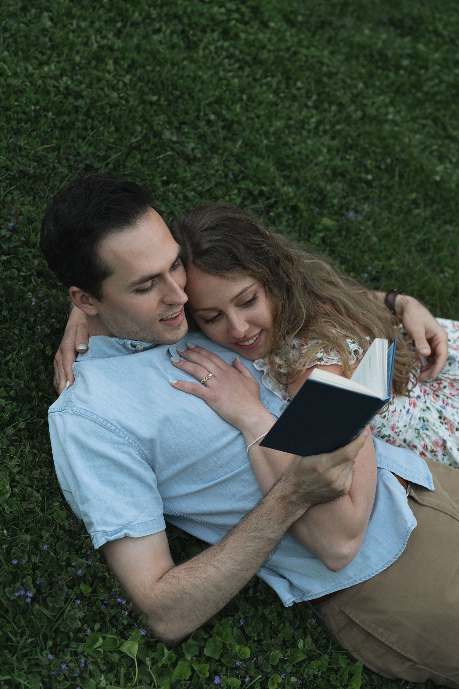 A couple relaxes on grass while reading a book together on a peaceful afternoon in the English countryside.
