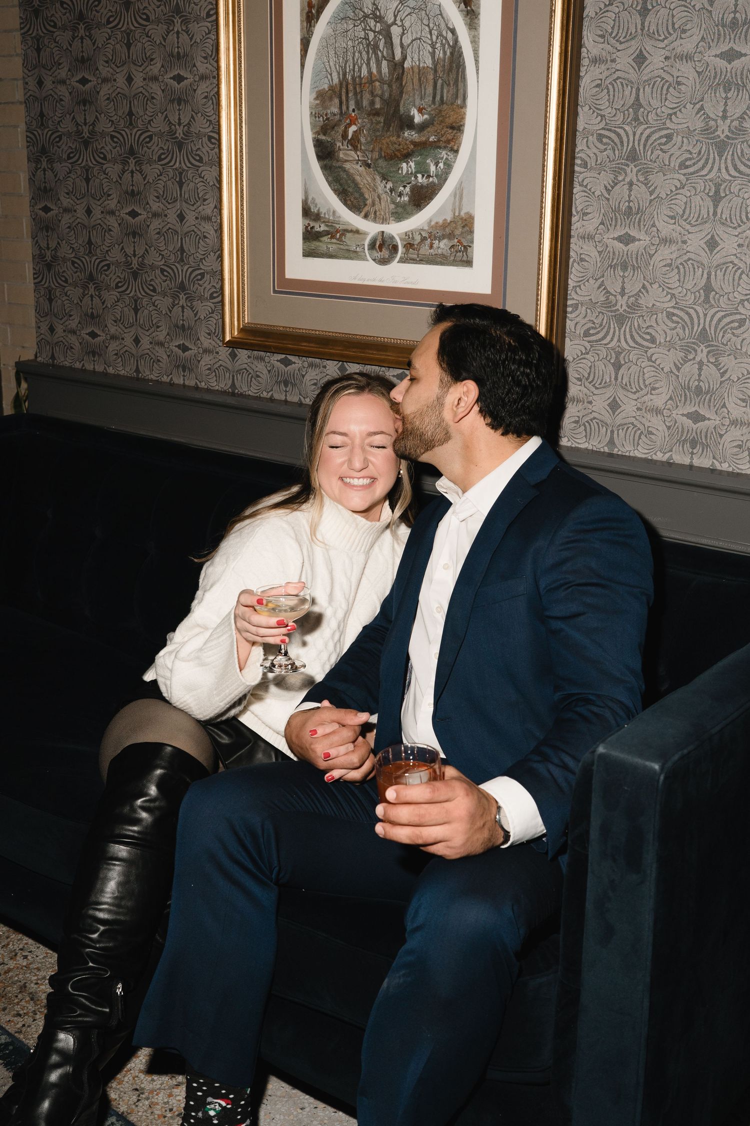 Two people share a laugh while sitting on a dark couch in an elegant room with patterned wallpaper in downtown Indianapolis