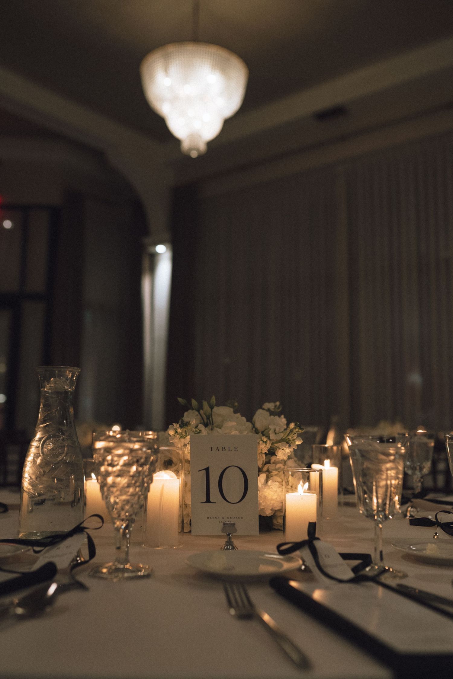 Candlelit wedding reception table settings with glowing glass votives and table numbers in an elegant dimly lit venue.