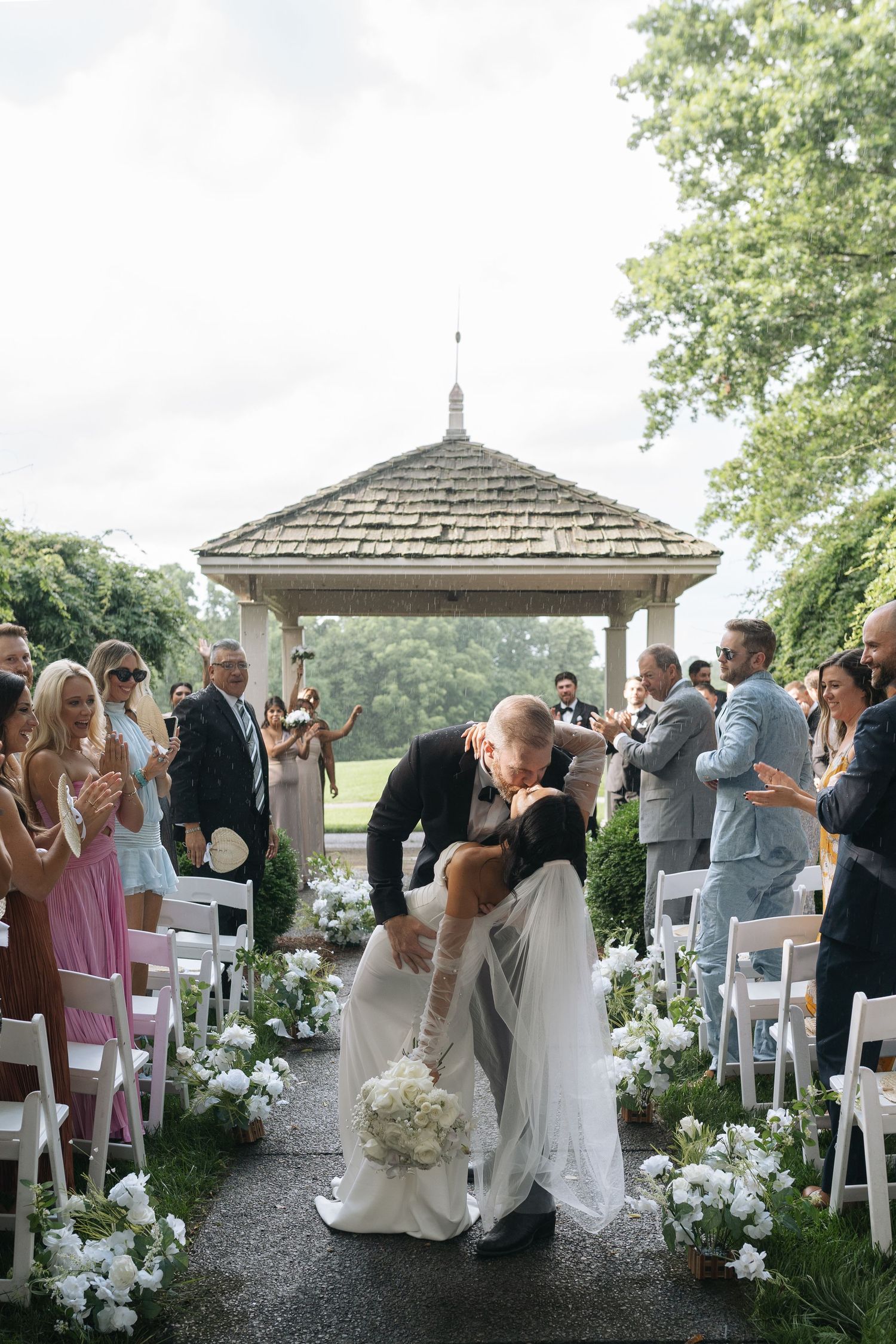 Outdoor wedding ceremony aisle kiss at a gazebo with guests surrounded by beautiful white floral decor in Nashville, Tennessee