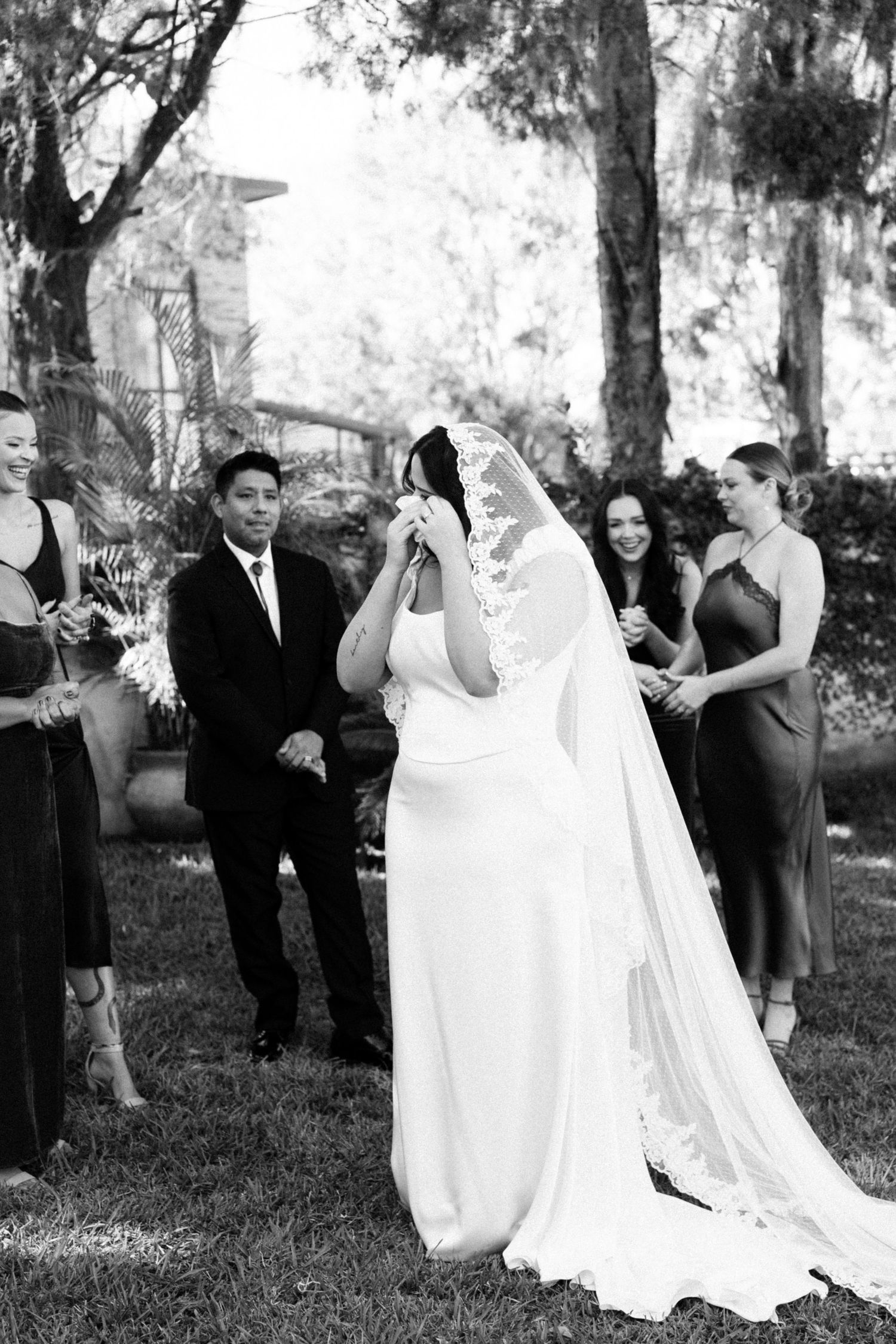 Black and white photo sequence of a joyful wedding party laughing and celebrating outdoors under trees.
