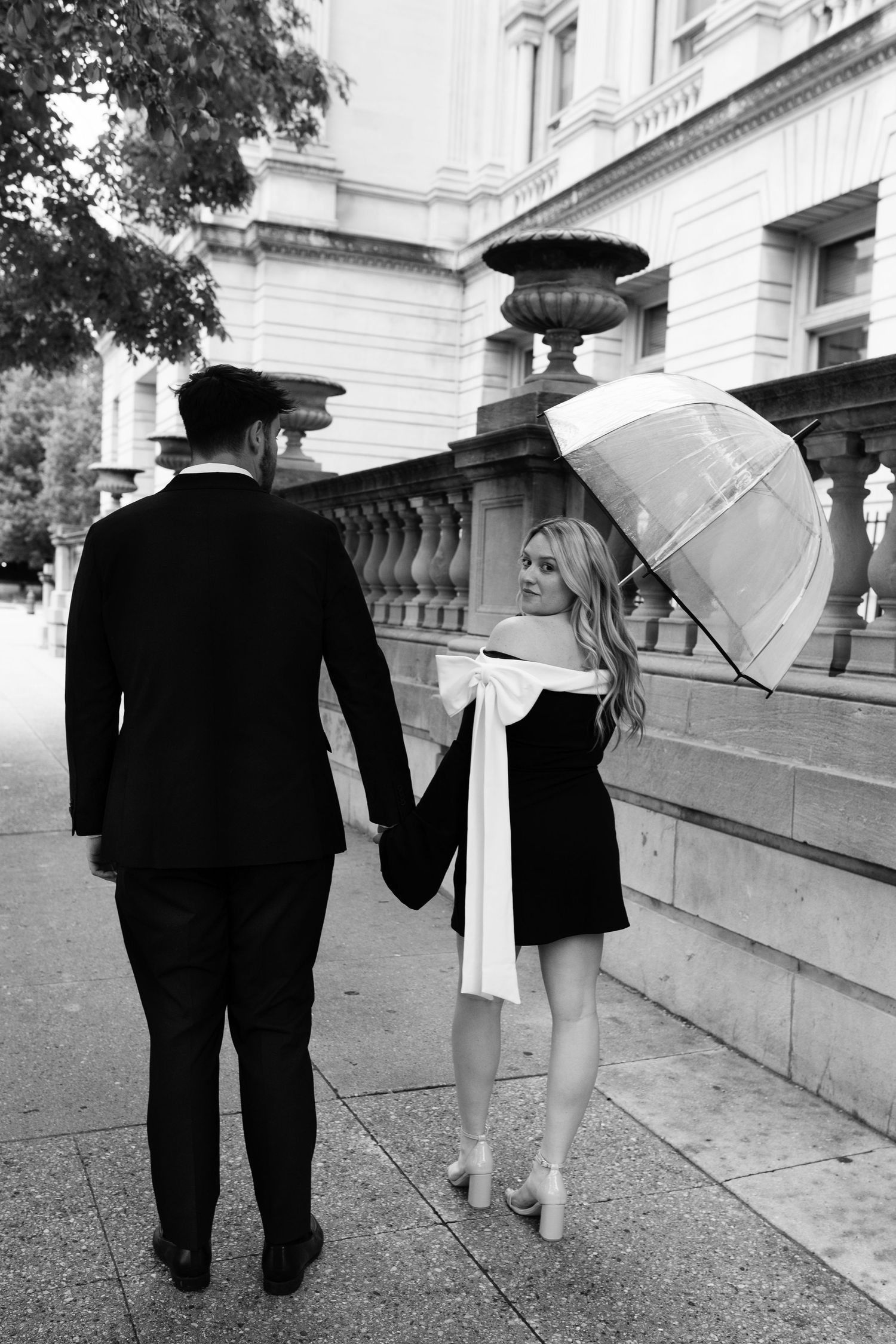 A sequence of black and white photos shows two people walking together with white umbrellas along an ornate stone path.
