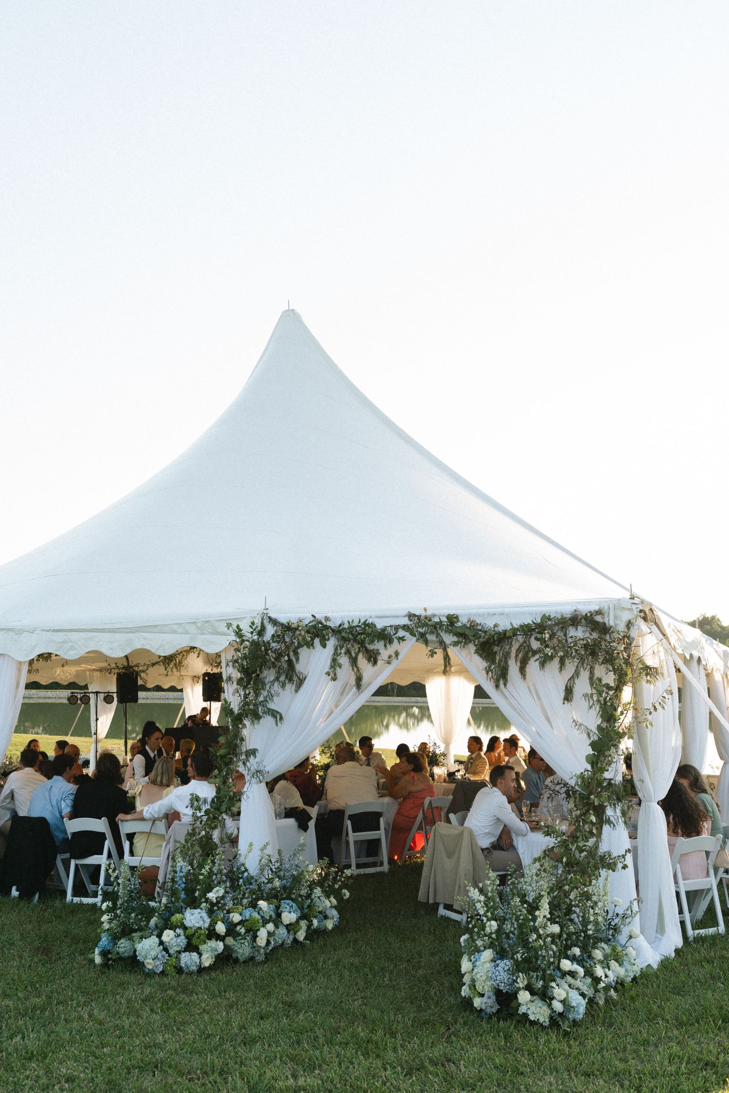 Elegant outdoor wedding reception under a white marquee tent adorned with greenery and white floral arrangements at dusk in Illinois