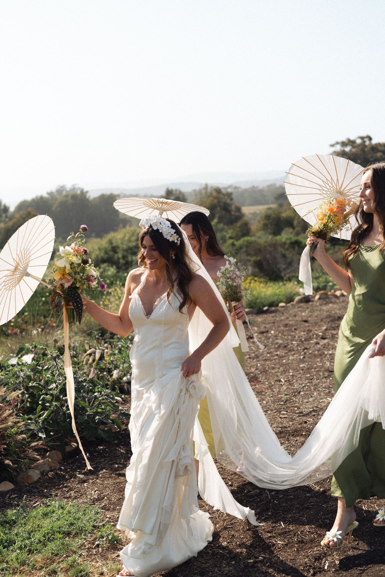 Wedding party with paper parasols pose outdoors on a sunny hillside path surrounded by greenery and nature in California