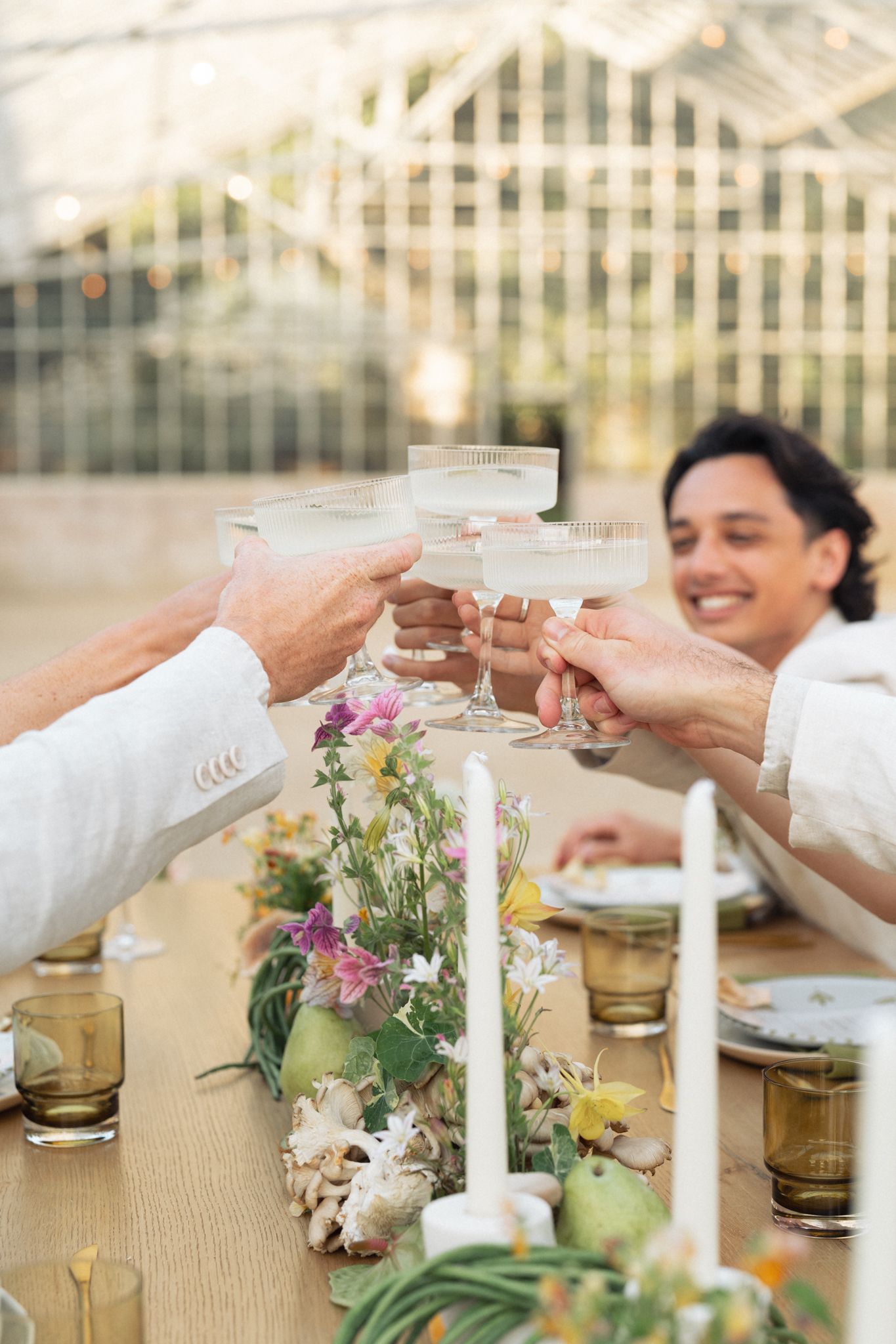 Toasting with wine glasses over a rustic table decorated with candlesticks and fresh flowers at an outdoor gathering in California