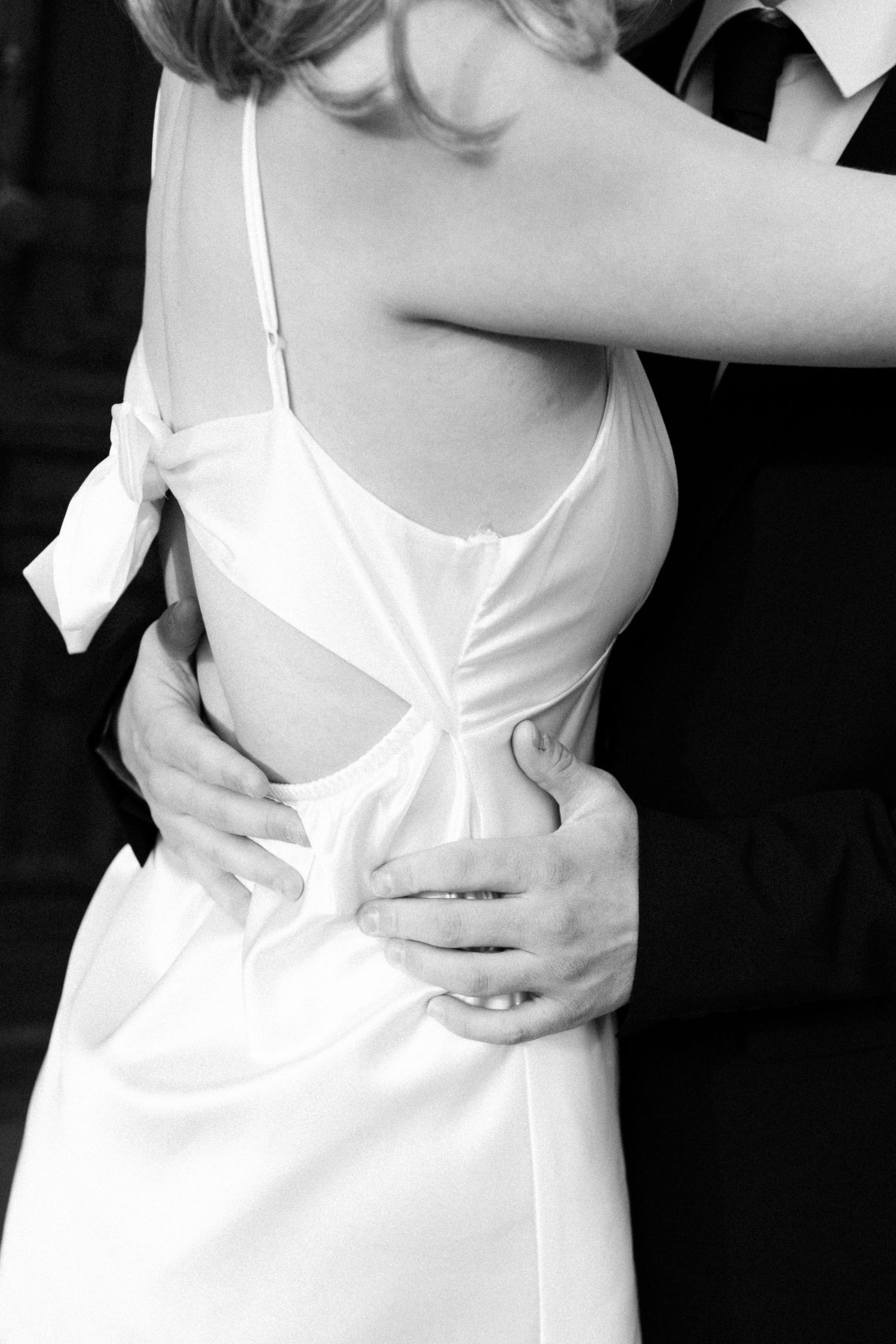 Black and white fashion photo showing close-up details of a white dress against dark background.