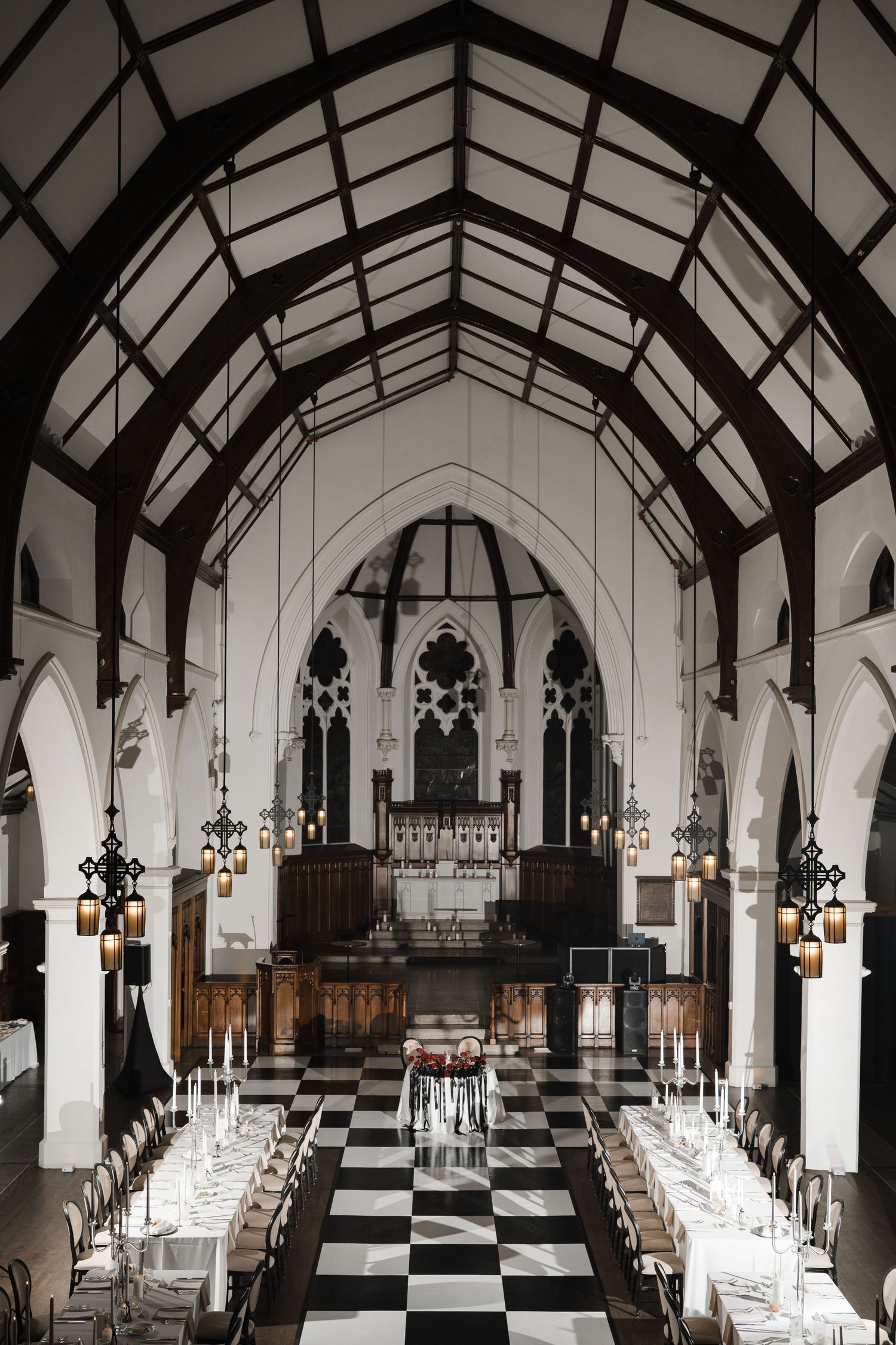 Elegant wedding reception in a Gothic-style church hall with black and white checkered floor and exposed wooden beams.