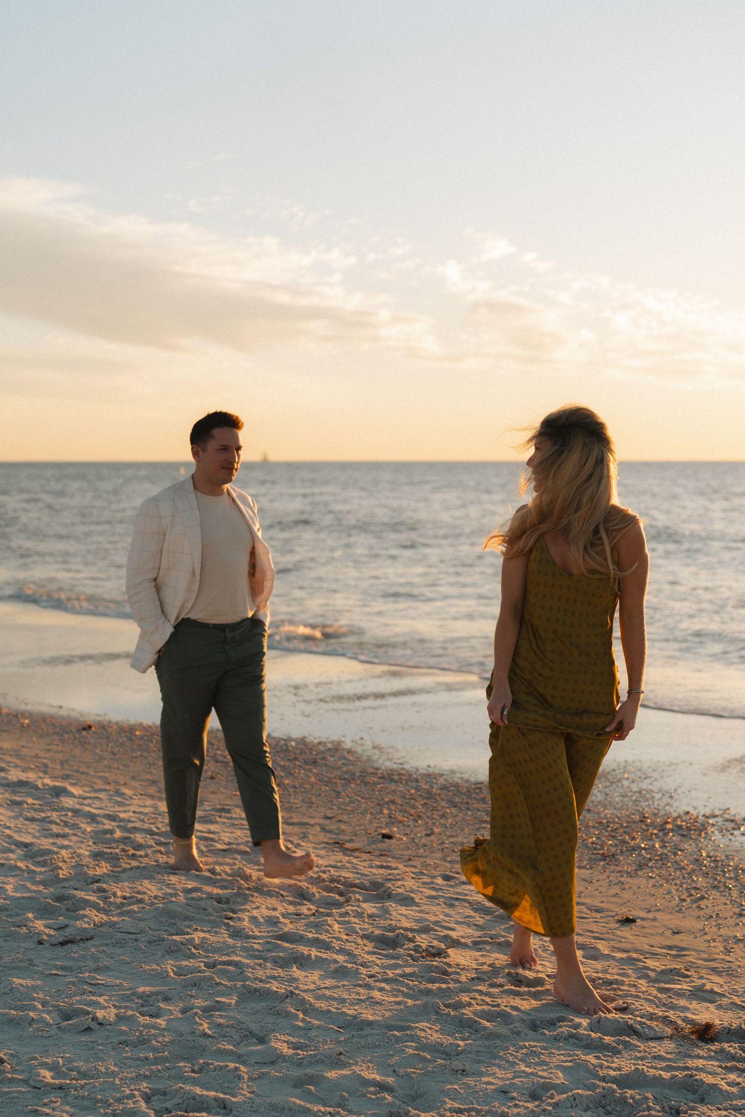 Two people walk along a sandy beach at sunset while waves roll onto the shore in Florida