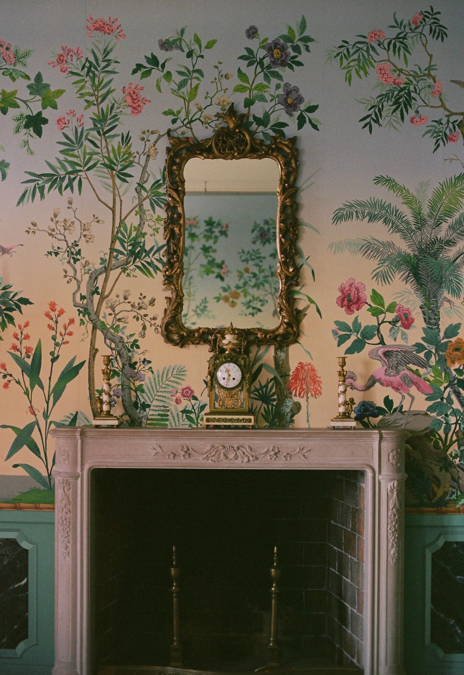 Vintage-style wall with delicate floral wallpaper design, ornate gold-framed mirrors, and white trim against a muted pink backdrop.