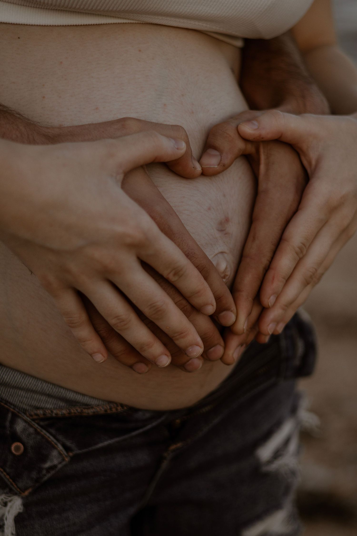 Close up of hands forming a heart shape over a pregnant belly.
