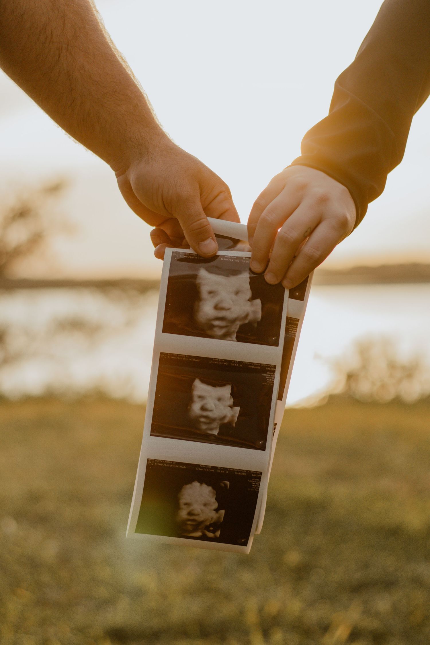 Hands holding ultrasound photos against a sunset backdrop.