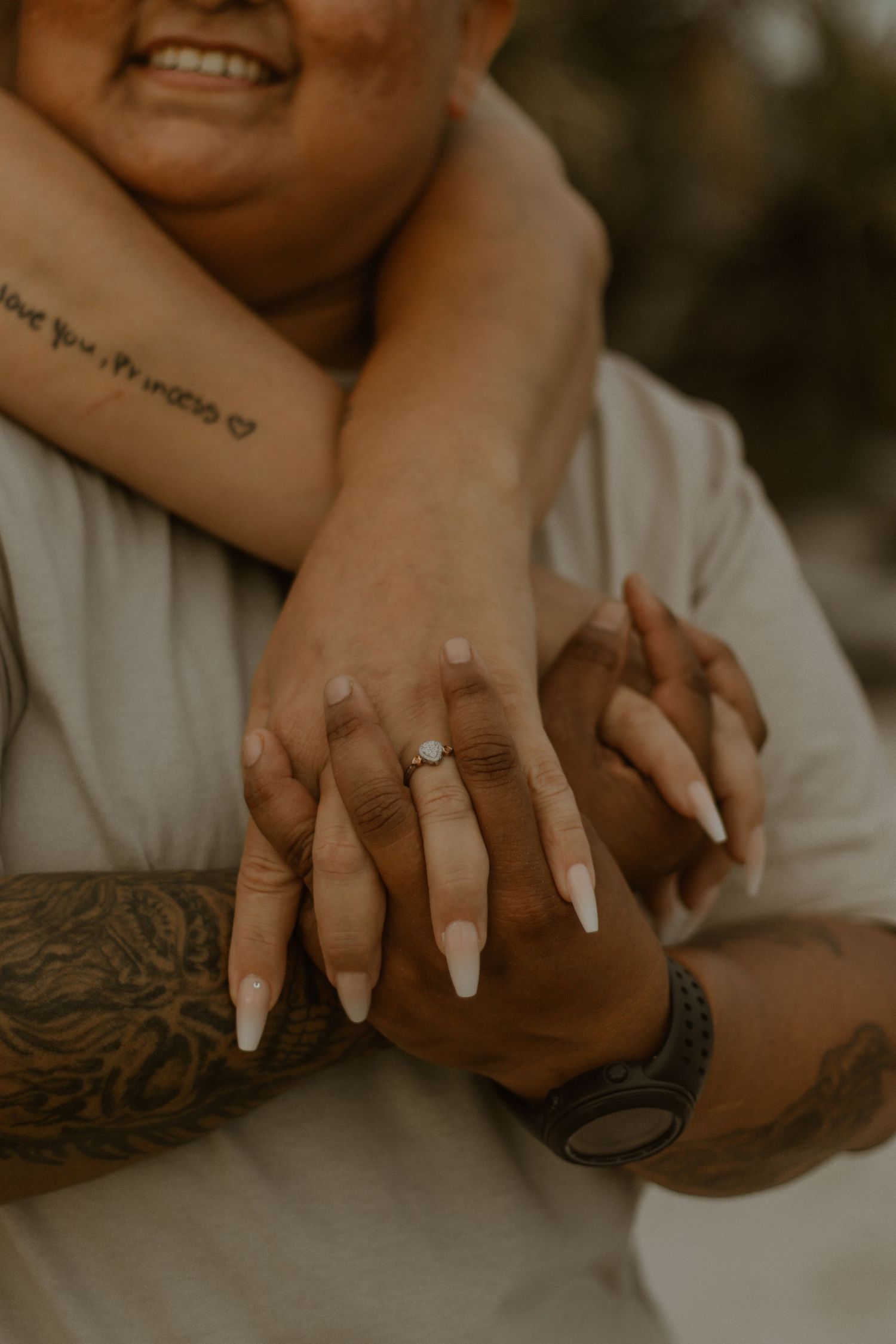 Close-up of intertwined hands with tattoos and manicured nails in warm lighting.