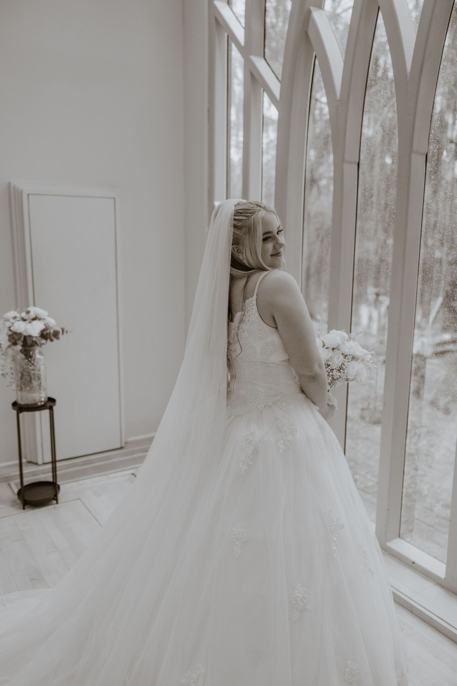 A radiant bride in a tulle ballgown poses by large arched windows.