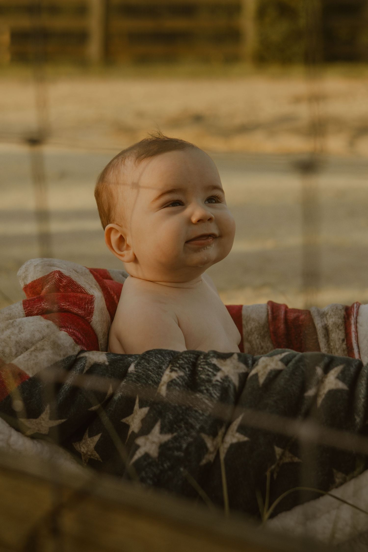Baby wrapped in an American flag blanket smiling during golden hour.