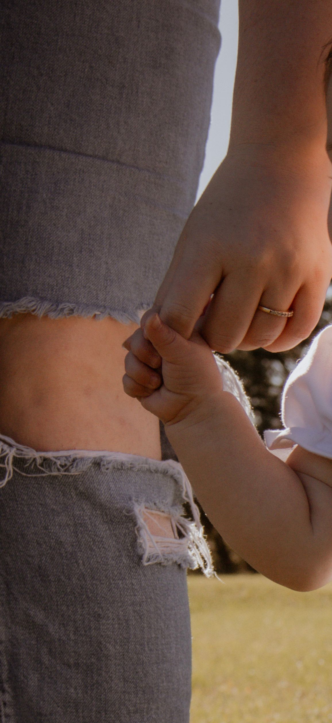 A tiny baby hand grasps an adult finger with a ring visible.