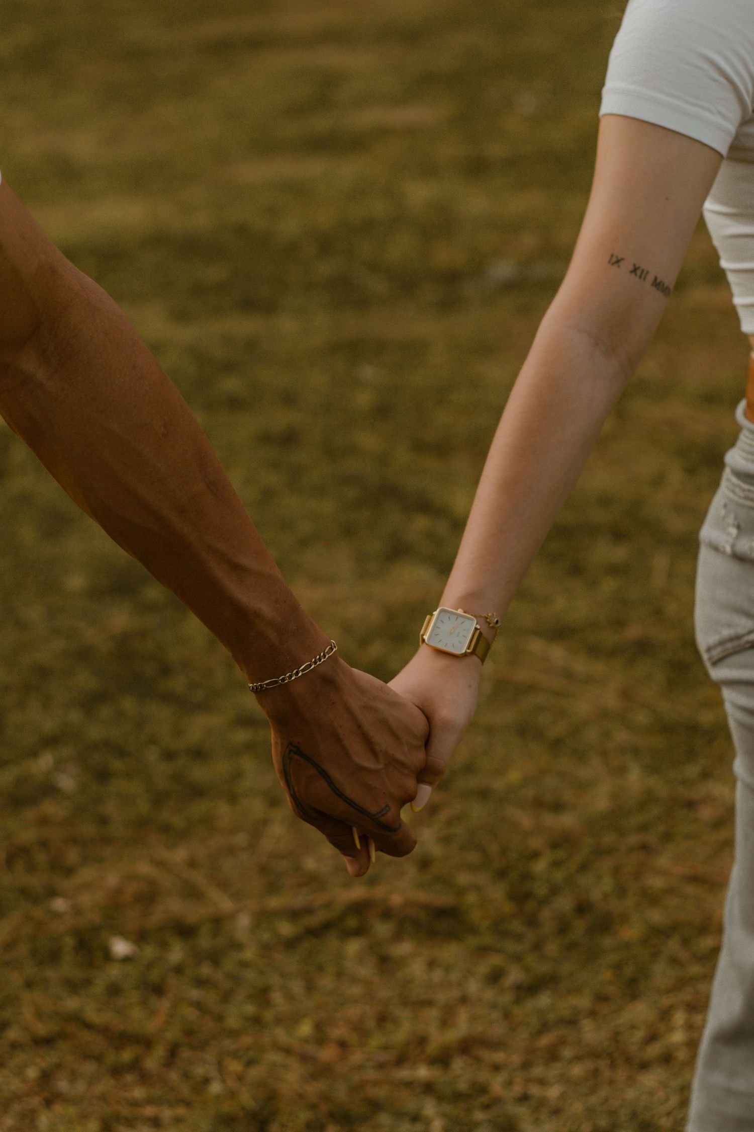 Two people holding hands in a grassy field at golden hour.
