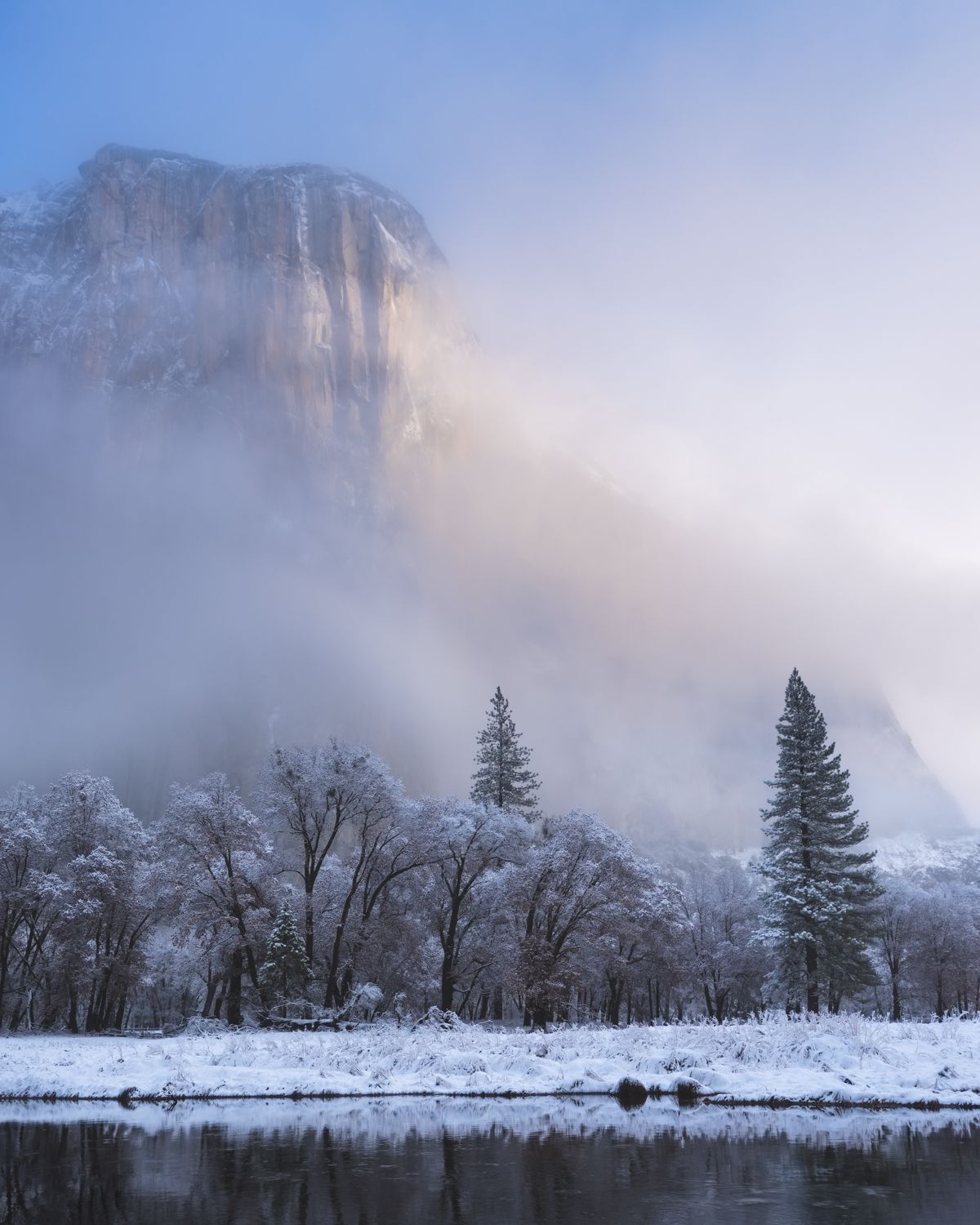 Snow-covered valley floor with misty mountains and evergreens in Yosemite National Park.