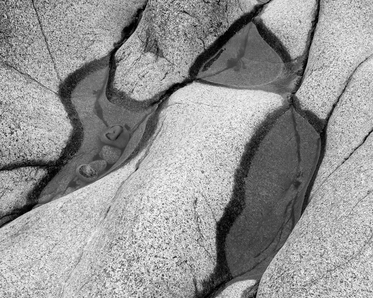 Black and white abstract photograph of water pools formed in granite rock formations creating organic shapes and patterns.