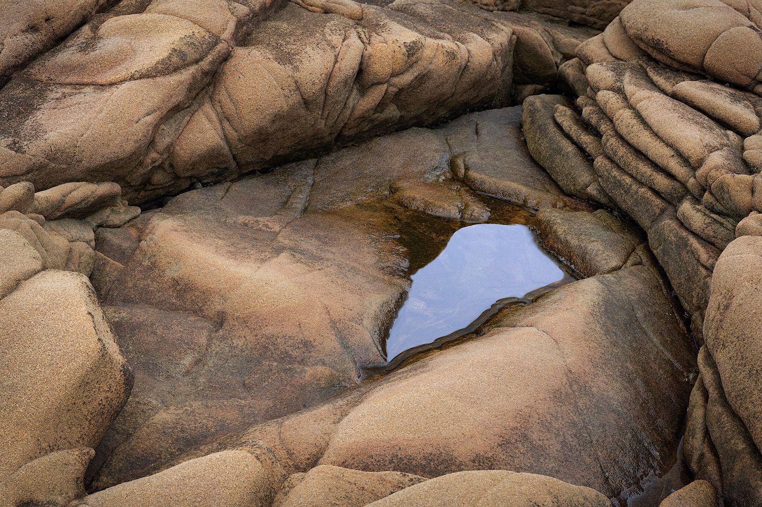 Natural rock formation creates a window-like opening revealing reflected blue sky in weathered sandstone.