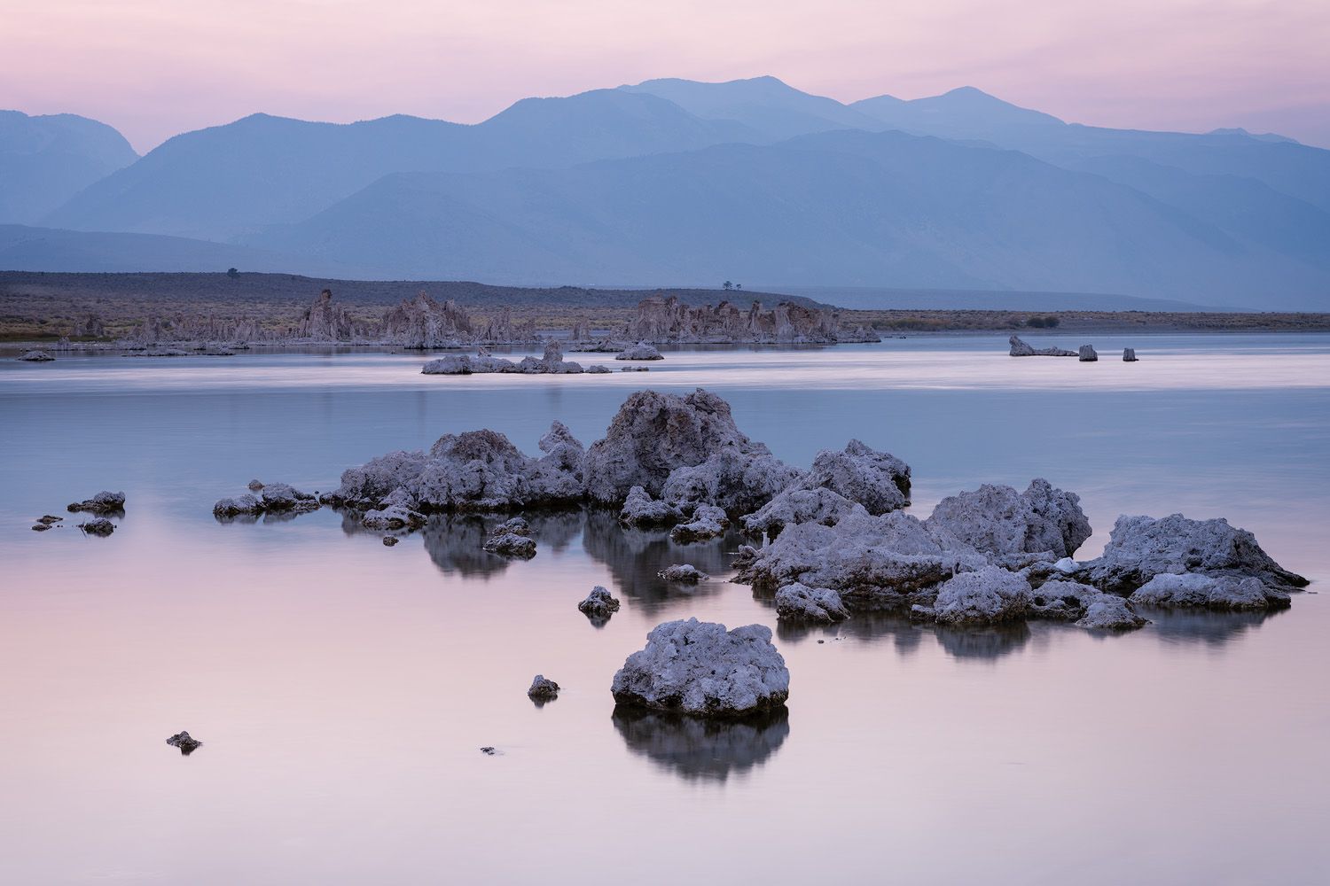 Tufa formations reflect in the still waters of Mono Lake at dusk.