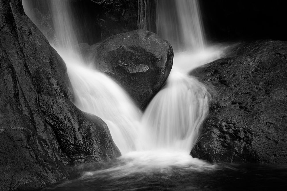 Black and white waterfall photograph showing water flowing dramatically between rock formations.