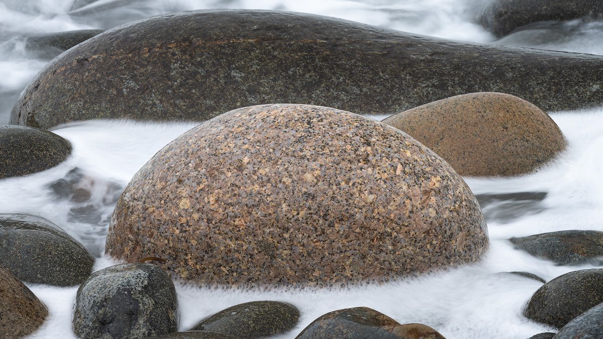 Smooth water flows over weathered stones in a rocky beach in Maine.