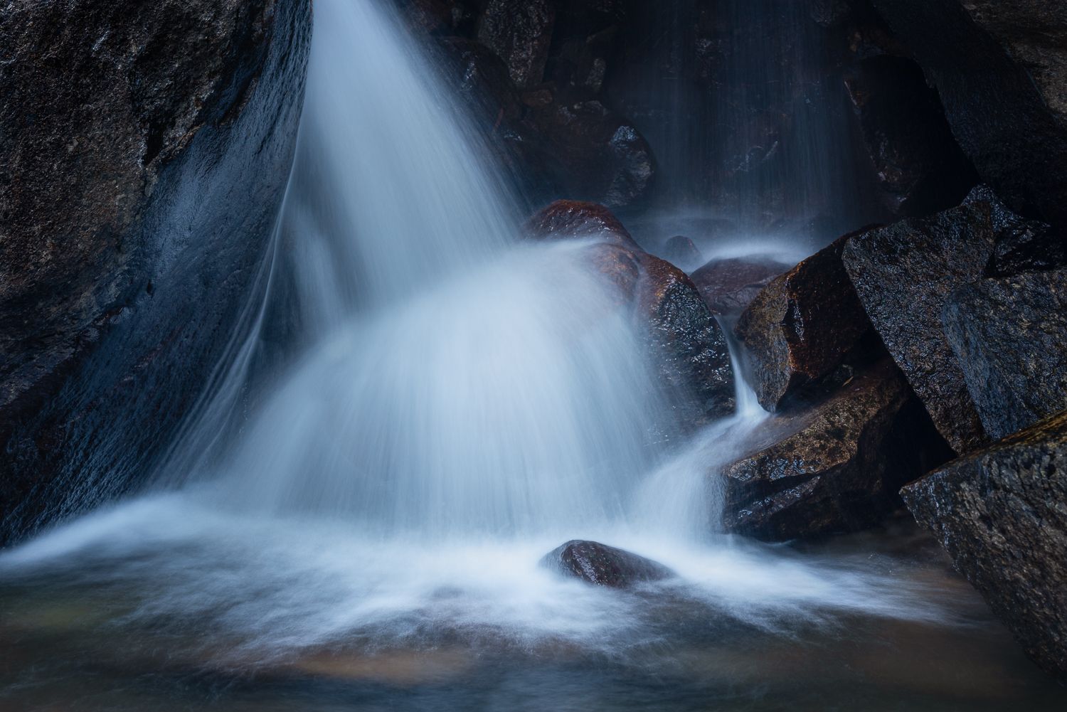 Ethereal waterfall flowing over dark rocks with smooth water motion captured in blue tones.