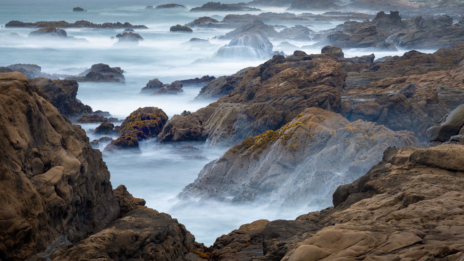 Misty seascape with waves crashing against rocky coastal outcrops.