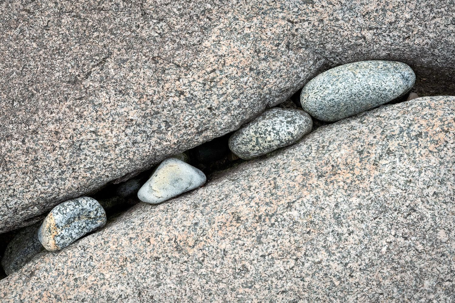 Smooth gray stones nestled in a curving crevice between granite rock formations.