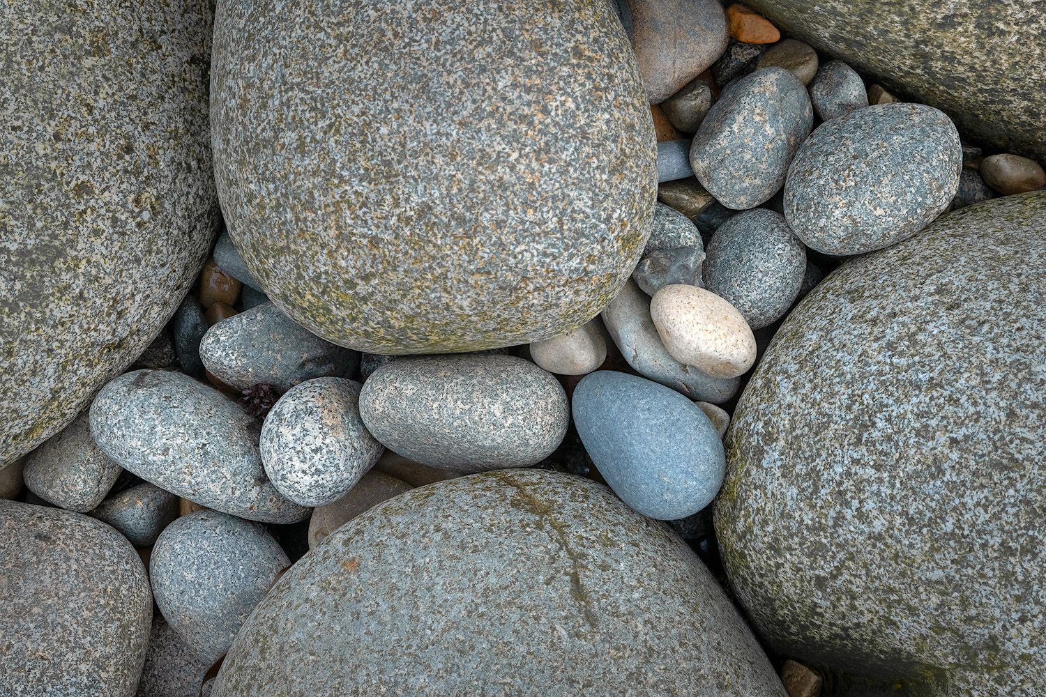 A collection of smooth gray river rocks and pebbles arranged on a rough textured surface.