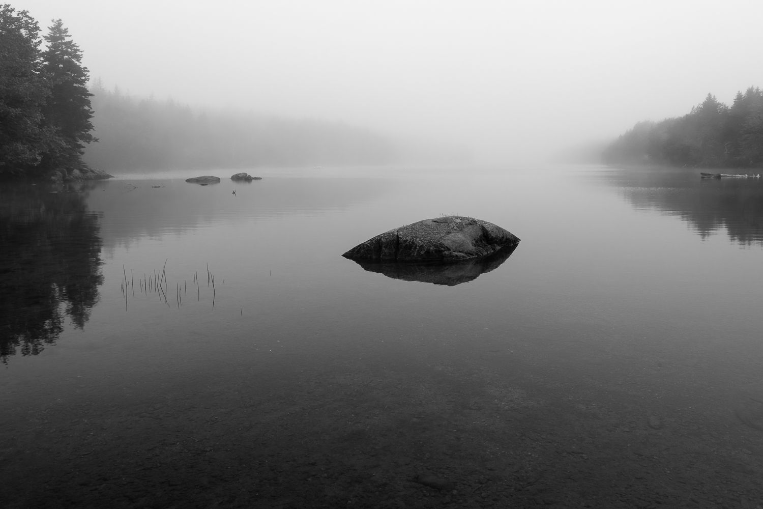 Minimalist black and white landscape of calm lake with single rock emerging from still water.